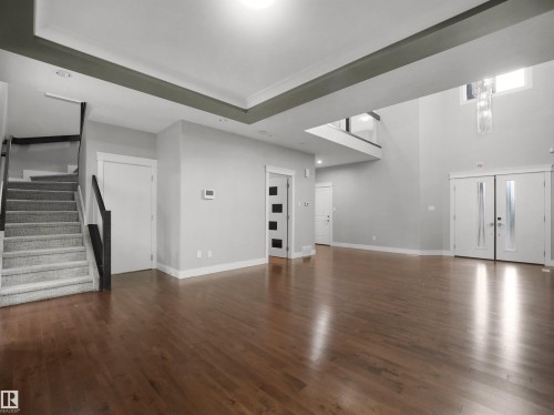Expansive open-concept space featuring rich wood-finish flooring and a grand double-height entry with a contemporary chandelier - 17020 62 Street Nw, Edmonton, AB - Indoor Photo Showing Other Room