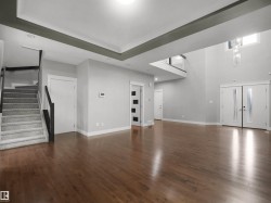 Expansive open-concept space featuring rich wood-finish flooring and a grand double-height entry with a contemporary chandelier - 