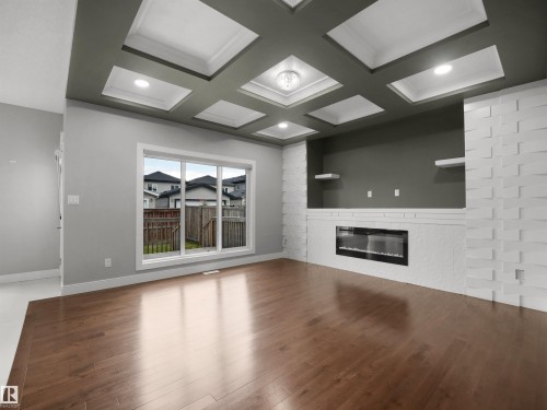 Coffered ceiling with recessed lighting, wood-finish flooring, white brick-patterned feature wall, built-in electric fireplace, and large sliding window - 17020 62 Street Nw, Edmonton, AB - Indoor Photo Showing Other Room With Fireplace