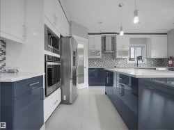 Modern kitchen featuring two-tone cabinetry, stainless steel appliances, a large island with a solid surface countertop, and a mosaic tile backsplash - 
