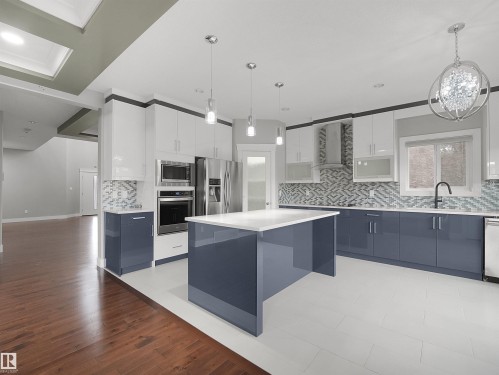Contemporary kitchen featuring a large central island, stainless steel appliances, a patterned tile backsplash, white tile flooring, and contrasting blue and white cabinetry - 17020 62 Street Nw, Edmonton, AB - Indoor Photo Showing Kitchen With Upgraded Kitchen