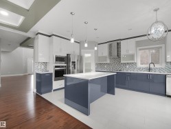 Contemporary kitchen featuring a large central island, stainless steel appliances, a patterned tile backsplash, white tile flooring, and contrasting blue and white cabinetry - 