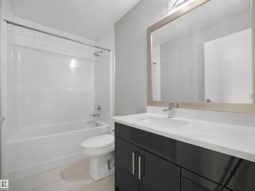Bathroom featuring a white bathtub, ceramic wall tiles, contemporary vanity with a white countertop and integrated sink, and a framed mirror - 17020 62 Street Nw, Edmonton, AB - Indoor Photo Showing Bathroom