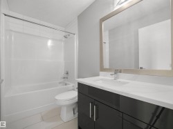 Bathroom featuring a white bathtub, ceramic wall tiles, contemporary vanity with a white countertop and integrated sink, and a framed mirror - 