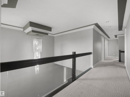 Open landing with a glass panel railing, dark wood-tone handrail, and patterned carpeting - 17020 62 Street Nw, Edmonton, AB - Indoor Photo Showing Other Room