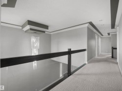 Open landing with a glass panel railing, dark wood-tone handrail, and patterned carpeting - 