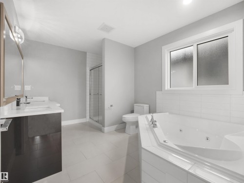 Dual vanity with undermount sinks, corner jetted tub, separate glass-enclosed shower, and large frosted window - 17020 62 Street Nw, Edmonton, AB - Indoor Photo Showing Bathroom