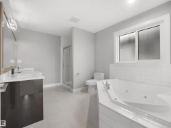 Dual vanity with undermount sinks, corner jetted tub, separate glass-enclosed shower, and large frosted window - 