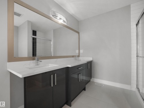 Dual vanity with white countertops, chrome fixtures, a broad framed mirror, and an illuminated light fixture - 17020 62 Street Nw, Edmonton, AB - Indoor Photo Showing Bathroom