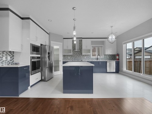 Open-concept kitchen with a central island, stainless steel appliances, large sliding glass doors, and two-tone cabinetry - 17020 62 Street Nw, Edmonton, AB - Indoor Photo Showing Kitchen With Upgraded Kitchen