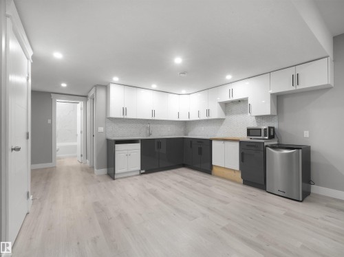 Corner kitchen with two-tone cabinetry, mosaic tile backsplash, and light wood-finish flooring - 17020 62 Street Nw, Edmonton, AB - Indoor Photo Showing Kitchen