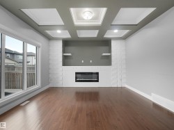 Wood-finish flooring, white brick fireplace surround, built-in electric fireplace, integrated shelving, coffered ceiling with recessed lighting - 