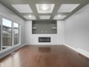 Wood-finish flooring, white brick fireplace surround, built-in electric fireplace, integrated shelving, coffered ceiling with recessed lighting - 17020 62 Street Nw, Edmonton, AB  - Indoor Photo Showing Other Room With Fireplace 
