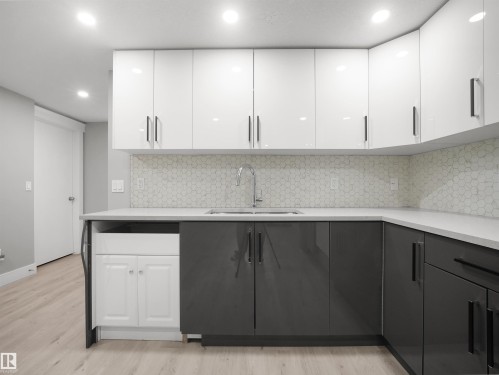 Contemporary kitchen featuring two-tone cabinetry, a white hexagonal tile backsplash, light wood-finish flooring, and recessed lighting - 17020 62 Street Nw, Edmonton, AB - Indoor Photo Showing Kitchen