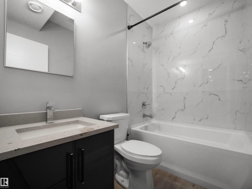 Bathroom featuring a dark wood-finish vanity with a light countertop, a rectangular sink with a chrome faucet, a white toilet, and a white tiled shower with a black shower rod - 17020 62 Street Nw, Edmonton, AB - Indoor Photo Showing Bathroom