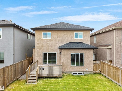 Rear exterior featuring stucco finish, a private wood fence, ground-level wood deck with steps, and multiple windows - 17020 62 Street Nw, Edmonton, AB - Outdoor With Exterior