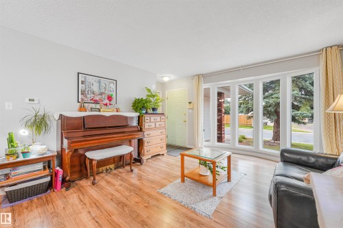 Bright living space featuring a bay window with multiple panes, wood-finish flooring, light gray wall tones, and a light-colored entry door - 18611 57 Avenue Nw, Edmonton, AB - Indoor Photo Showing Living Room
