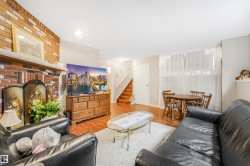 Living area featuring a brick fireplace, wood-finish flooring, staircase, and a dining alcove with a large window - 