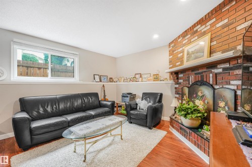 Brick fireplace with a white mantel, wood-finish flooring, recessed lighting, and a window with white trim - 18611 57 Avenue Nw, Edmonton, AB - Indoor Photo Showing Living Room With Fireplace
