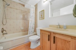 Bathroom featuring a light wood-finish vanity with a built-in sink, a rectangular mirror, a shower-over-tub combination with tiled surround, and wood-finish flooring - 