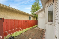 Private outdoor patio featuring brick paver flooring, a red wood privacy fence, and integrated landscaping - 