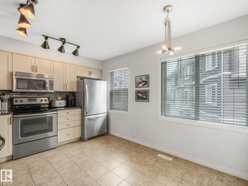 Kitchen featuring stainless steel appliances, light wood-finish cabinetry, tile flooring, and a mosaic tile backsplash - #21 1140 Chappelle Bv Sw, Edmonton, AB - Indoor Photo Showing Kitchen