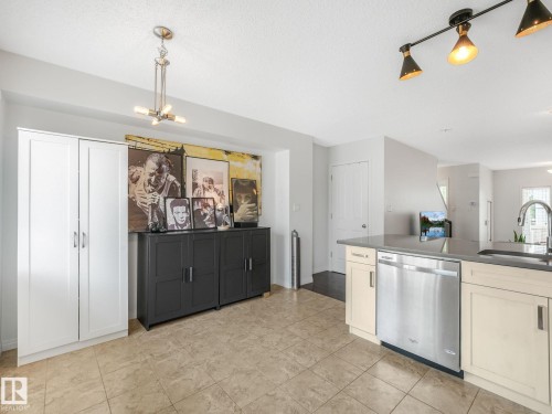 Kitchen area featuring tile flooring, track lighting, and a kitchen island with an undermount sink and stainless steel dishwasher - #21 1140 Chappelle Bv Sw, Edmonton, AB - Indoor Photo Showing Kitchen
