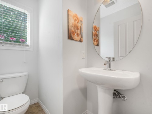 Pedestal sink with chrome faucet and an oval frameless mirror - #21 1140 Chappelle Bv Sw, Edmonton, AB - Indoor Photo Showing Bathroom