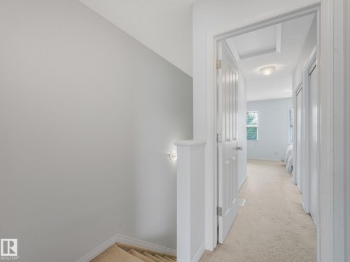 Upper-level hallway featuring carpet flooring, crisp white trim, and a wall-mounted sconce - #21 1140 Chappelle Bv Sw, Edmonton, AB - Indoor Photo Showing Other Room