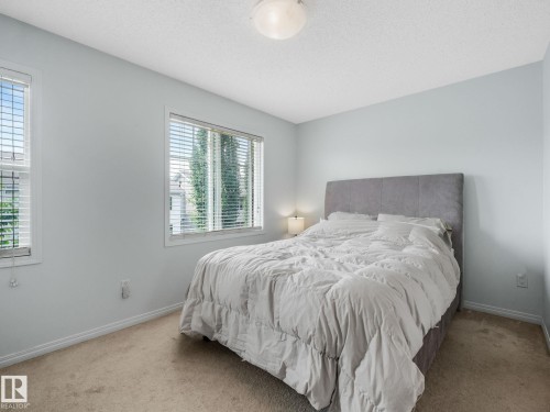 Bedroom featuring two windows with horizontal blinds, light-colored carpeting, a textured ceiling, and pale blue wall paint - #21 1140 Chappelle Bv Sw, Edmonton, AB - Indoor Photo Showing Bedroom