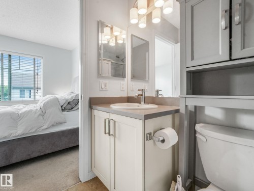 Bathroom vanity with an undermount sink, a chrome faucet, and a wall-mounted mirror with overhead lighting - #21 1140 Chappelle Bv Sw, Edmonton, AB - Indoor Photo Showing Bathroom