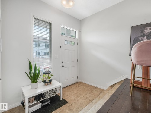 Entryway featuring a white paneled door with transom window, tile flooring, an adjacent vertical window with blinds, and ceiling-mounted lighting - #21 1140 Chappelle Bv Sw, Edmonton, AB - Indoor Photo Showing Other Room
