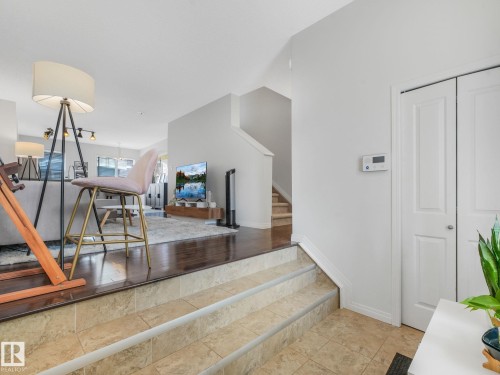 Split-level interior featuring tile flooring at entry, two steps up to wood-finish flooring, white walls, and a staircase with wood-finish treads - #21 1140 Chappelle Bv Sw, Edmonton, AB - Indoor Photo Showing Other Room
