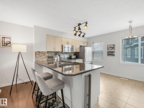 Kitchen featuring a peninsula with countertop seating, stainless steel appliances, a mosaic tile backsplash, and light-toned cabinetry - #21 1140 Chappelle Bv Sw, Edmonton, AB - Indoor Photo Showing Kitchen With Double Sink