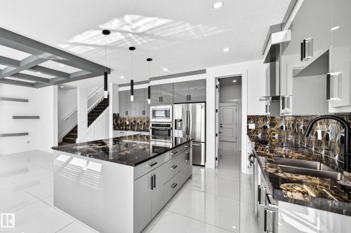 Gourmet kitchen featuring a large central island, integrated stainless steel appliances, modern pendant lighting, and a unique hexagonal tile backsplash - 3101 Soleil Boulevard, Beaumont, AB - Indoor Photo Showing Kitchen With Upgraded Kitchen
