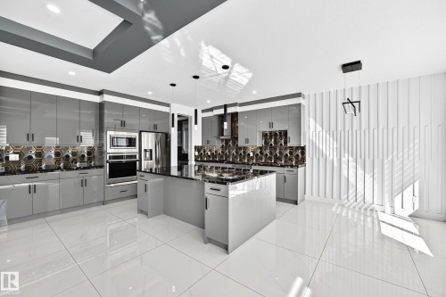 Contemporary kitchen featuring a large central island, gray high-gloss cabinetry, integrated stainless steel appliances, geometric backsplash, and polished tile flooring - 3101 Soleil Boulevard, Beaumont, AB - Indoor Photo Showing Kitchen With Upgraded Kitchen