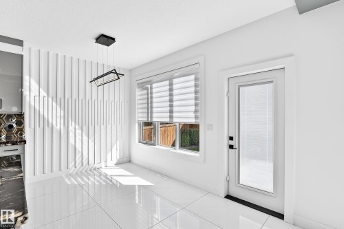 White tile flooring, full-light exterior door, modern chandelier, window with horizontal blinds, and a decorative accent wall - 3101 Soleil Boulevard, Beaumont, AB - Indoor Photo Showing Other Room