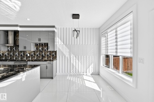 White tile flooring, contemporary pendant lighting, window with horizontal blinds, textured wall paneling, and a kitchen island with dark countertops - 3101 Soleil Boulevard, Beaumont, AB - Indoor