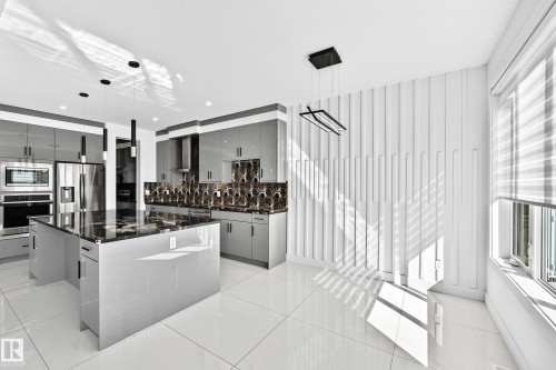 Gourmet kitchen featuring a large island with dark stone countertops, sleek gray cabinetry, stainless steel appliances, and a decorative backsplash - 3101 Soleil Boulevard, Beaumont, AB - Indoor