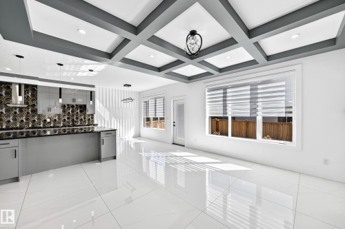 White tile flooring, coffered ceiling with recessed lighting, kitchen island with dark countertop, gloss gray cabinetry, and geometric tile backsplash - 3101 Soleil Boulevard, Beaumont, AB - Indoor Photo Showing Other Room