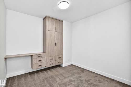 Built-in storage solutions with wood-finish cabinetry and black hardware, complemented by a floating desk surface and wall-mounted overhead lighting - 3101 Soleil Boulevard, Beaumont, AB - Indoor Photo Showing Other Room