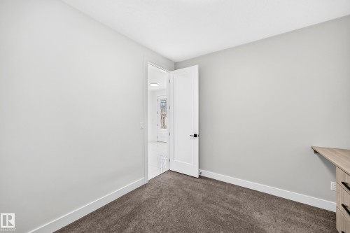 Neutral wall tones, dark textured carpeting, and a built-in wood-finish corner desk - 3101 Soleil Boulevard, Beaumont, AB - Indoor Photo Showing Other Room