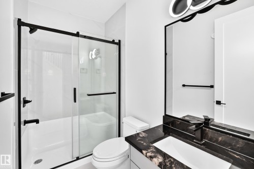 Shower-over-tub combination with sliding glass doors, black-framed mirror, contemporary vanity lighting, black granite-style countertop, and integrated rectangular sink - 3101 Soleil Boulevard, Beaumont, AB - Indoor Photo Showing Bathroom