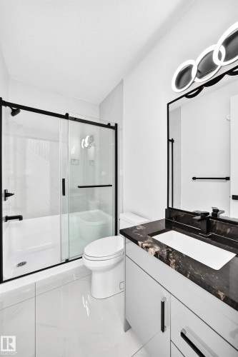 White tile flooring, black-framed sliding glass shower door, dark stone-finish vanity countertop, white undermount sink, and contemporary vanity lighting fixture - 3101 Soleil Boulevard, Beaumont, AB - Indoor Photo Showing Bathroom