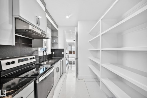 Modern galley kitchen featuring stainless steel appliances, black countertops, and white flat-panel cabinetry - 3101 Soleil Boulevard, Beaumont, AB - Indoor Photo Showing Kitchen With Double Sink