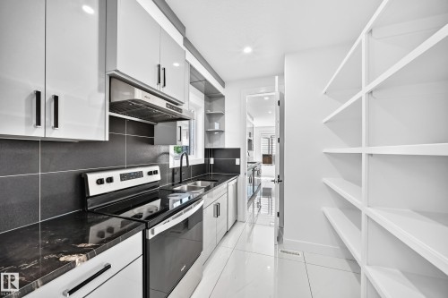 Contemporary kitchen featuring glossy white cabinetry, dark stone countertops, stainless steel appliances, and a full-height pantry with integrated shelving - 3101 Soleil Boulevard, Beaumont, AB - Indoor Photo Showing Kitchen With Double Sink With Upgraded Kitchen