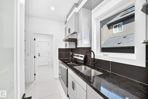 Modern kitchen featuring a dual-basin stainless steel sink, black-finish faucet, dark stone countertops, and white flat-panel cabinetry - 3101 Soleil Boulevard, Beaumont, AB - Indoor Photo Showing Kitchen With Double Sink