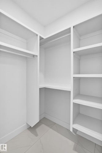Built-in closet system with shelving, hanging rods, and light-toned tile flooring - 3101 Soleil Boulevard, Beaumont, AB - Indoor With Storage