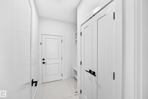 White paneled doors with matte black hardware, tiled flooring, and built-in shelving - 3101 Soleil Boulevard, Beaumont, AB - Indoor Photo Showing Other Room