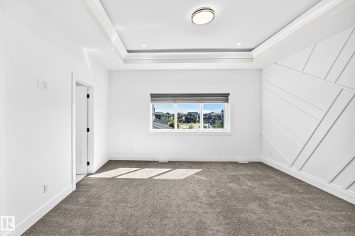 Tray ceiling with recessed lighting, integrated flush mount fixture, textured accent wall, window with roller shade, and plush carpeting - 3101 Soleil Boulevard, Beaumont, AB - Indoor Photo Showing Other Room